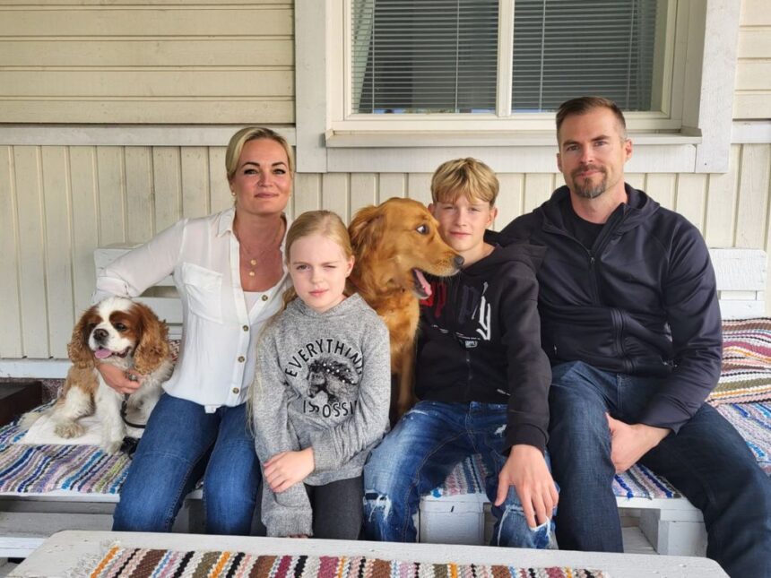 Asumiskokeilijat_Mannermaa Perhe ja koirat poseeraavat talon edustalla penkillä.